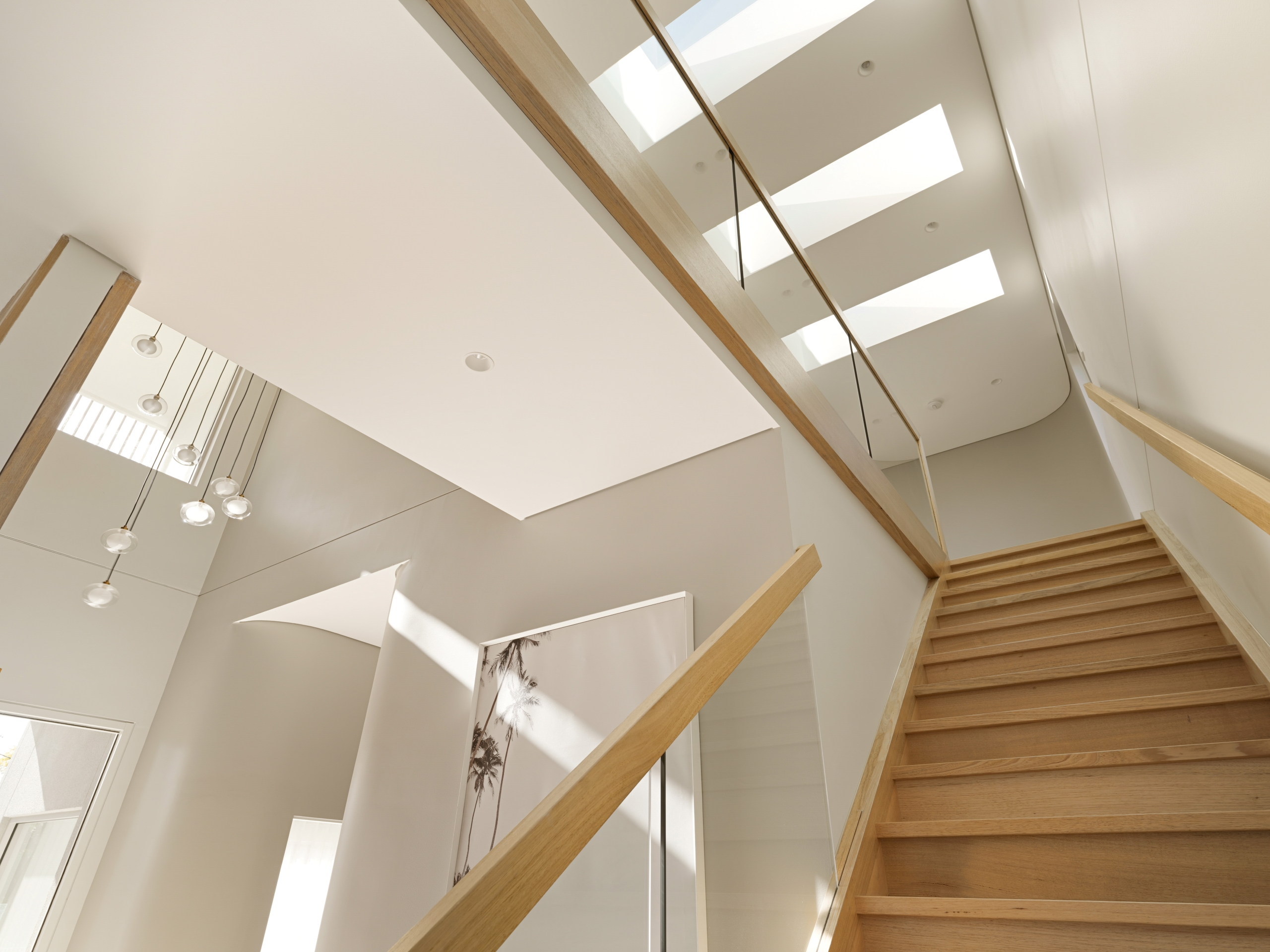 A contemporary home interior featuring a sleek wooden staircase, high ceilings, and strategically placed skylights that flood the space with natural light.